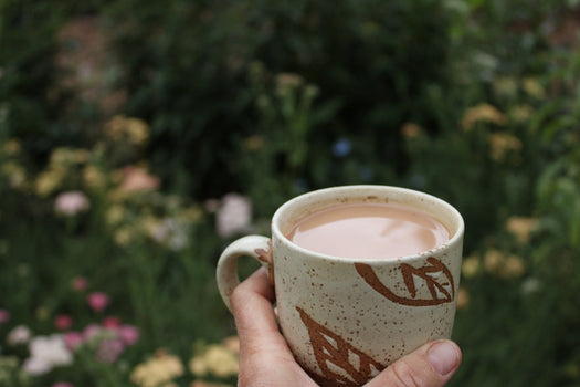 Holding a creamy cup of black tea in the garden with flowers in the background