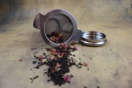 a picture of our two piece stainless steel tea strainer on its side with our assam rose black tea pouring out