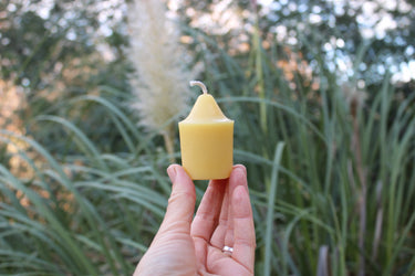 Single unscented yellow beeswax votive candle held in hand