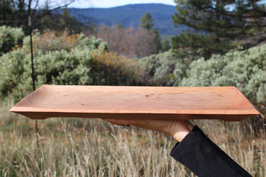 Tan oak wooden serving tray with recessed center held outdoors