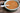 Orange-brown bone broth with herbs in ceramic bowl