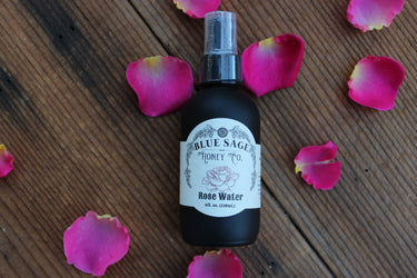 Bottle of Blue Sage Honey Co. Rose Water with pink rose petals on a wooden surface