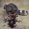 Spilling stainless steel tea strainer with loose leaf tea and rose petals showing fine mesh detail