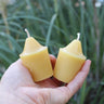 Hand holding two pure yellow beeswax votive candles with cotton wicks