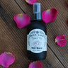 Bottle of Blue Sage Honey Co. Rose Water with pink rose petals on a wooden surface